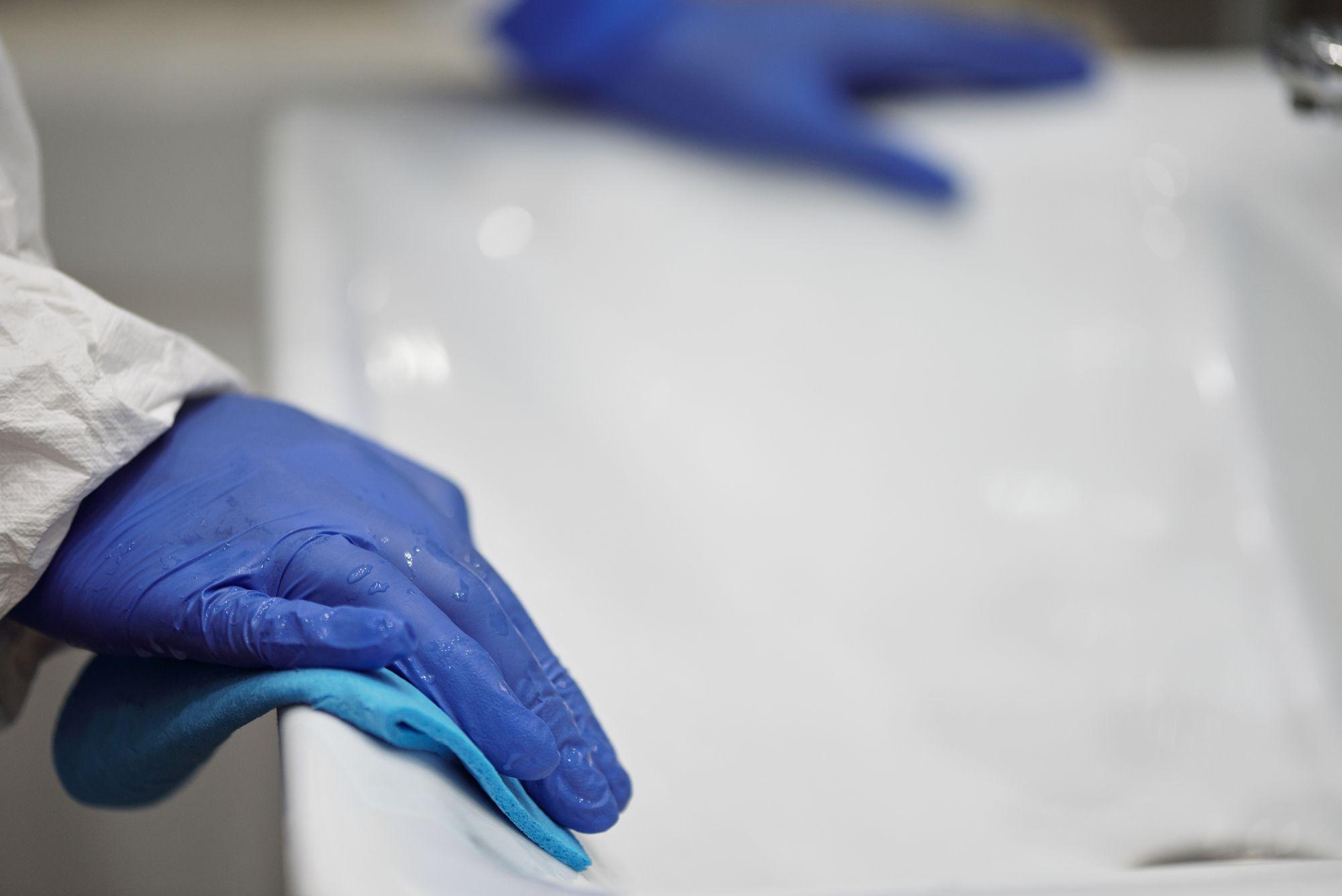 Gloved hands wiping a white sink